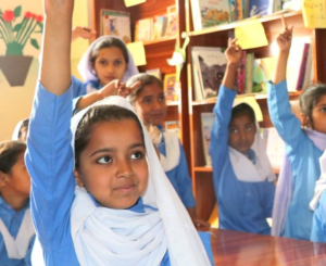 Young girls excitedly raise their hands to answer a question while learning in schools supported by DIL