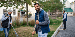 A young man volunteer with team looking at camera and cleaning up street, community service concept - CAF America Champions the Localization Agenda